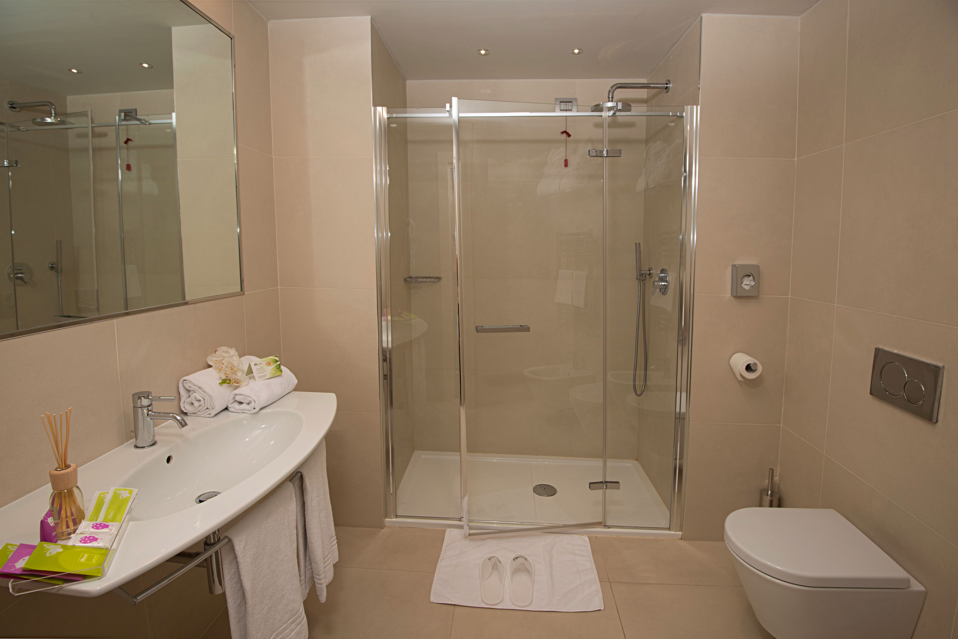 Un baño moderno con ducha envuelta en vidrio, un lavamanos blanco con espejo y un inodoro.