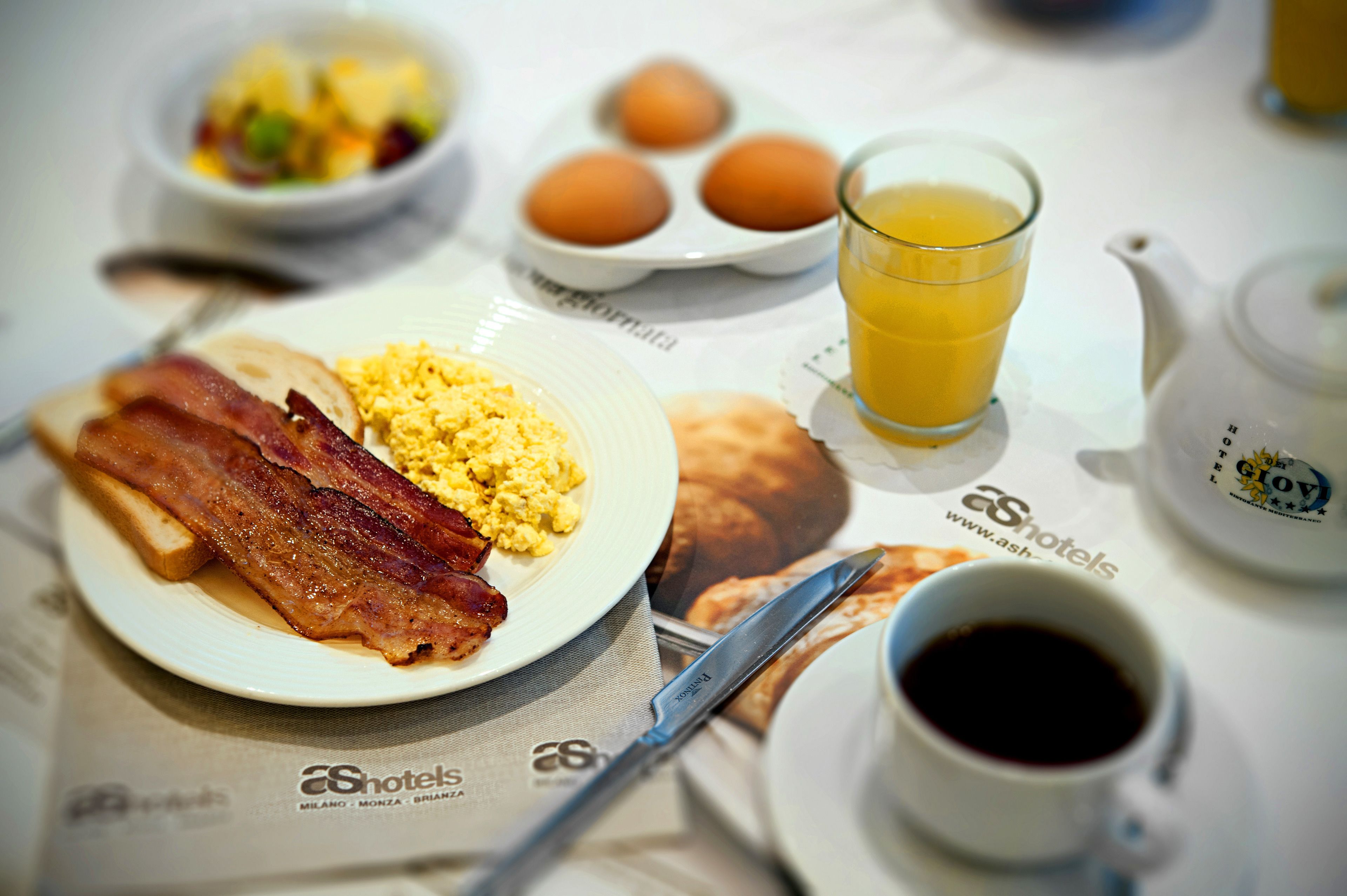 A breakfast table with eggs, bacon, toast, a glass of orange juice, and a cup of coffee.