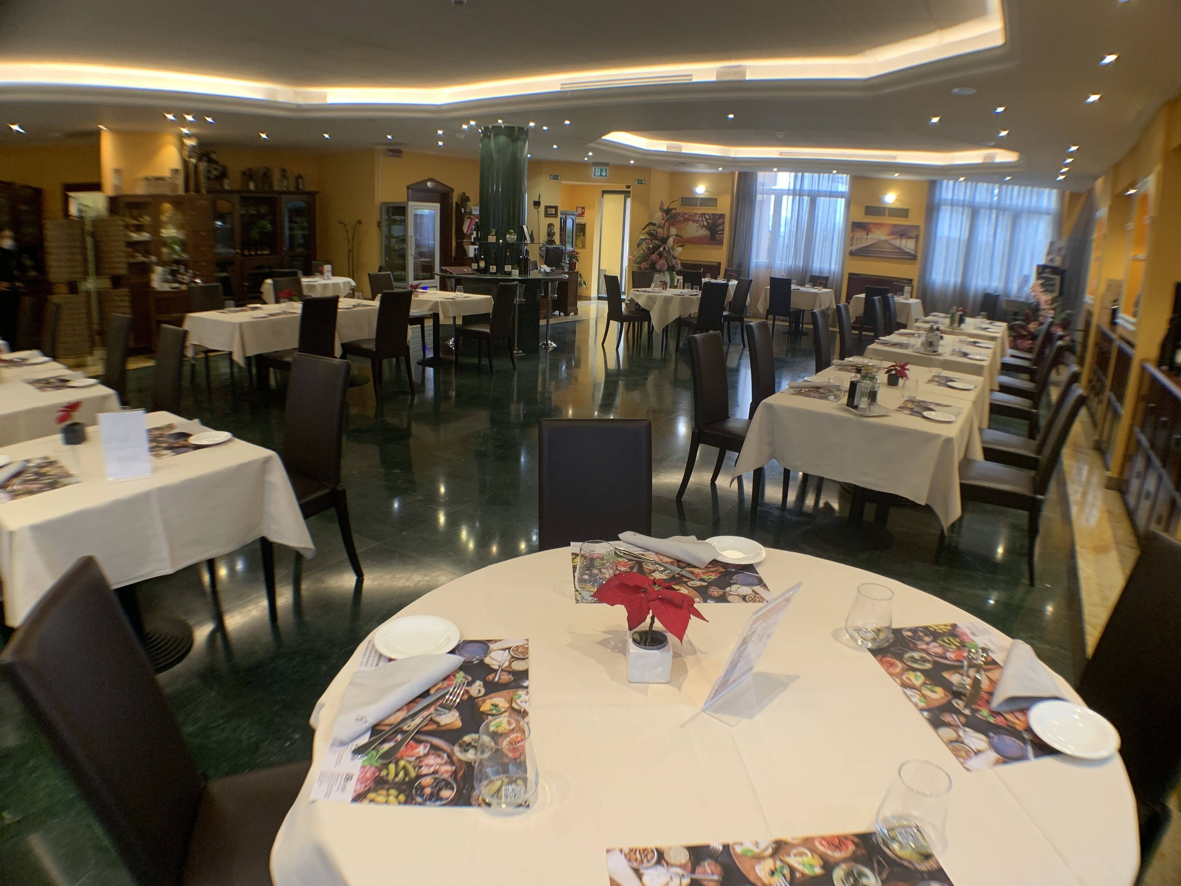 A spacious restaurant with multiple round tables, each set with white tablecloths, plates, and cutlery.