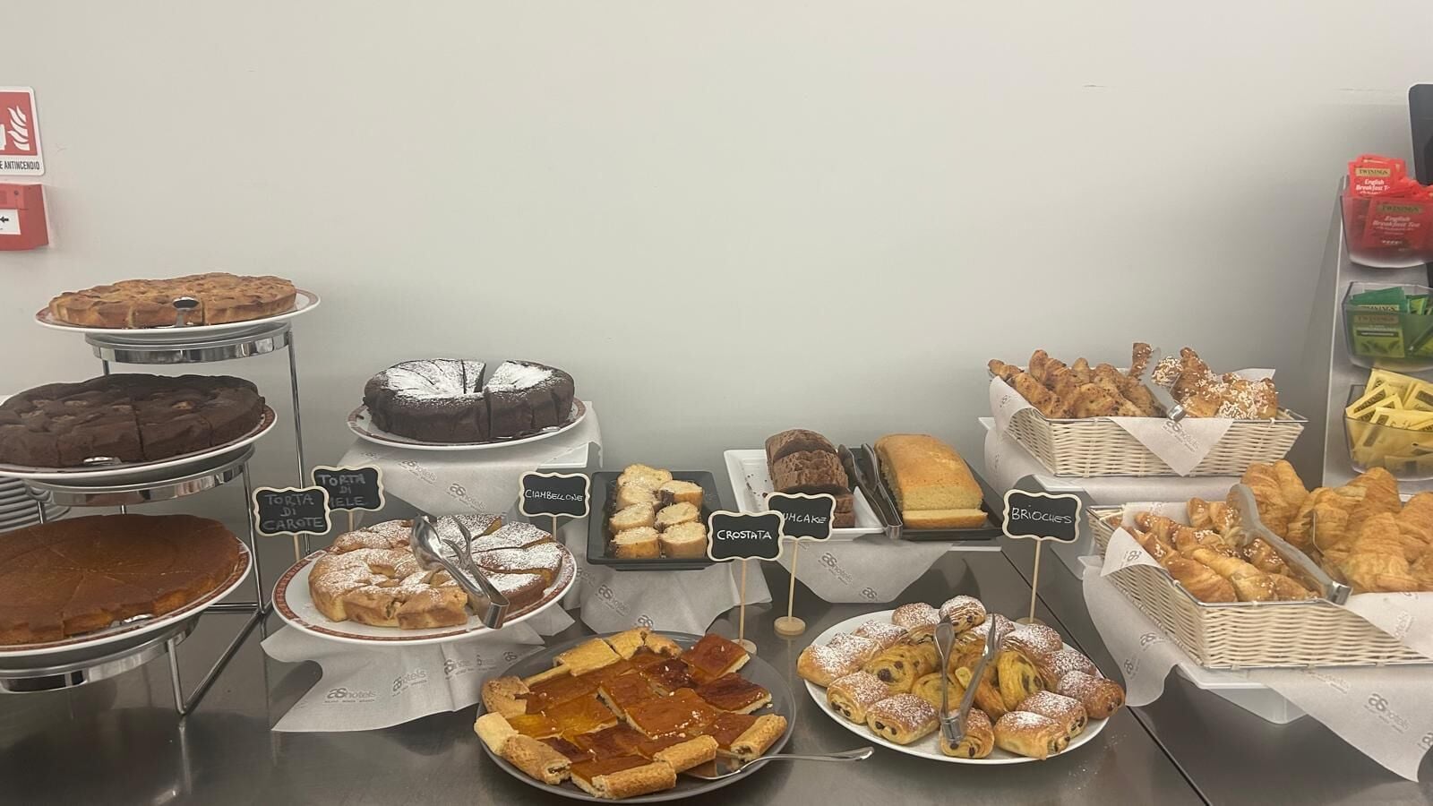 A variety of baked goods displayed on a counter with labels indicating different types of pastries and cakes.