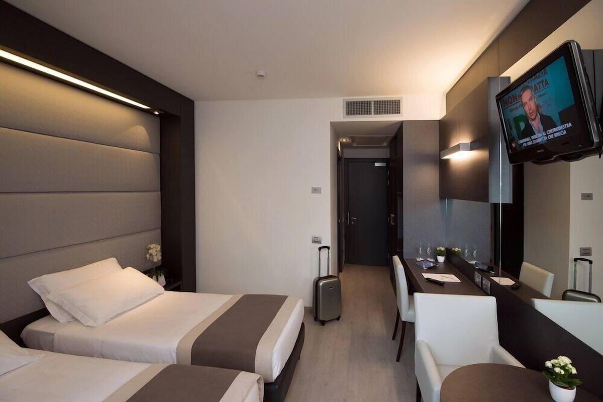 Ein Hotelzimmer mit zwei Betten, einem Schreibtisch, einem Stuhl, einem Fernseher und einer Badezimmertür.