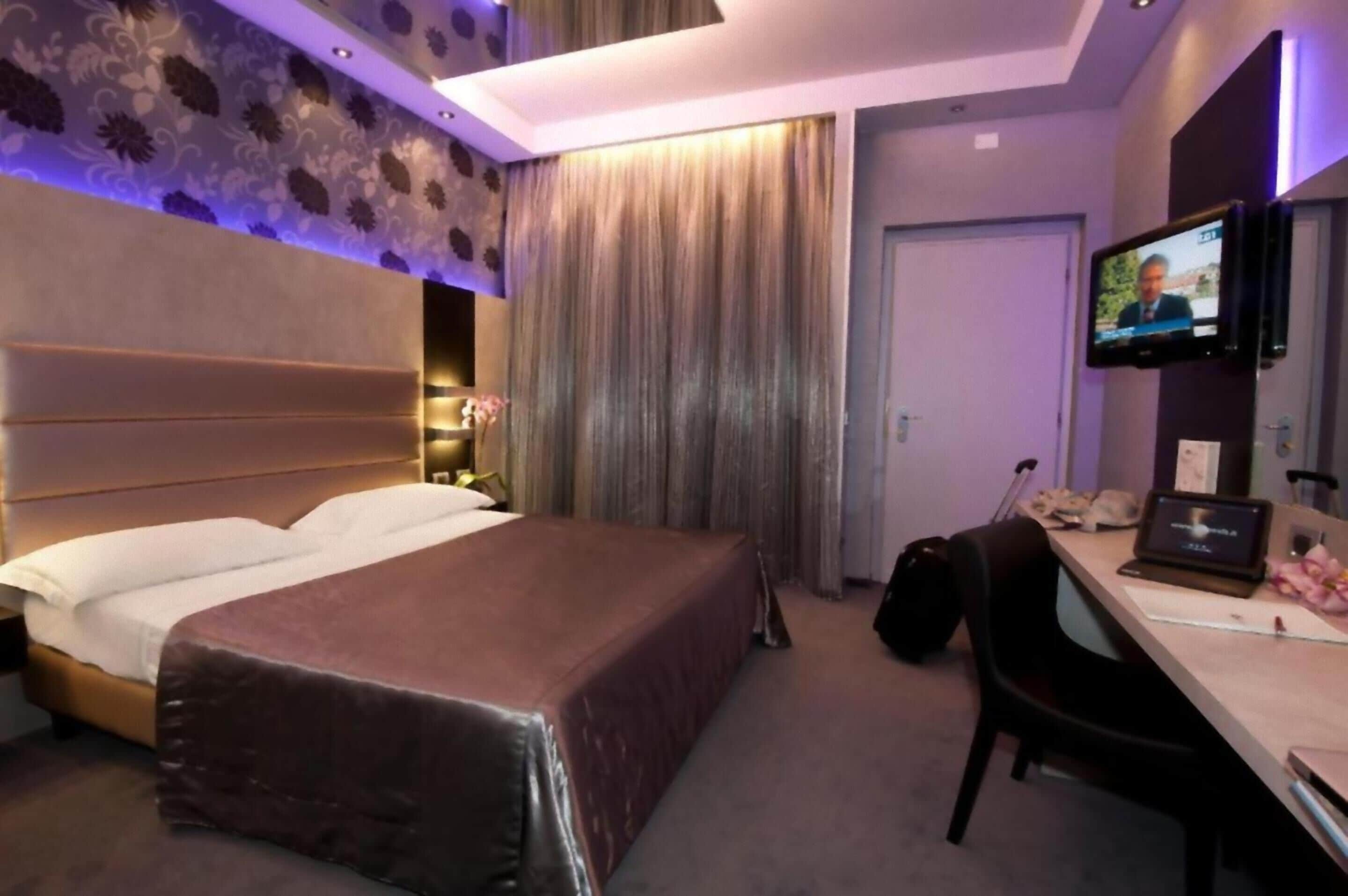 A hotel room with a large bed, a desk with a laptop, a television, and a curtain.