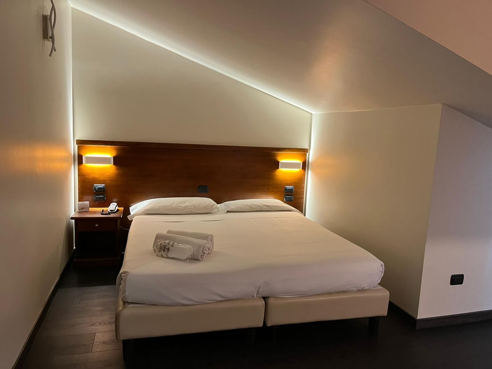 Une chambre d’hôtel moderne avec un lit bien fait, des lampes de chevet et une tête de lit en bois.