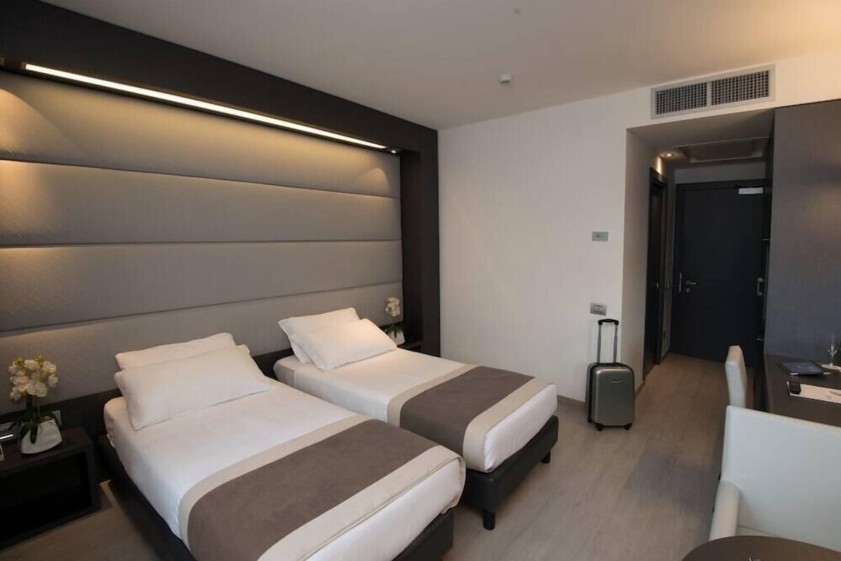Ein Hotelzimmer mit zwei Betten, einem Schreibtisch, einem Stuhl, einem Koffer und einer T ür.