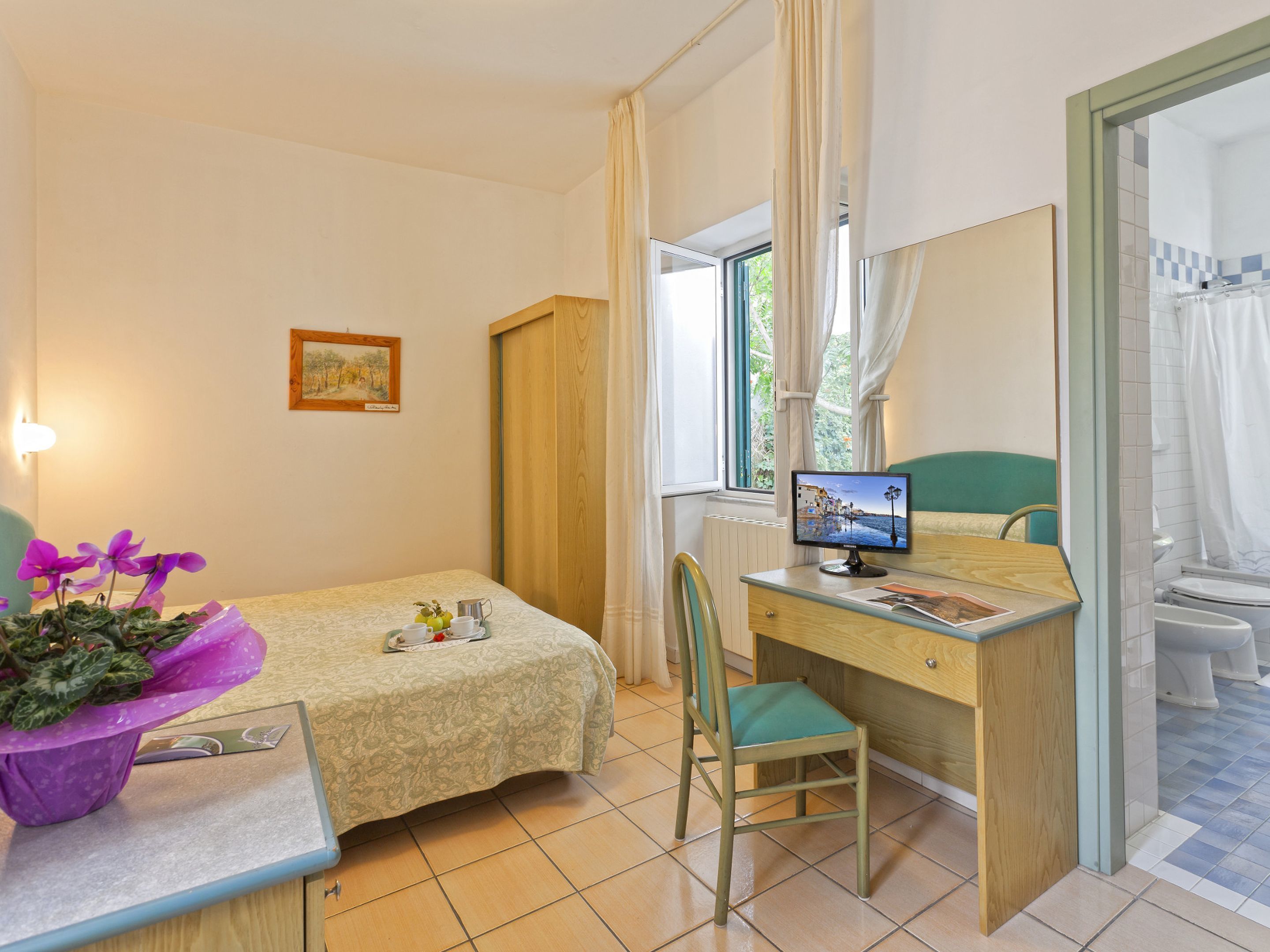 A room with a bed, a desk with a computer, a chair, a window with curtains, and a radiator.
