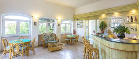 A spacious room with a bar area, multiple seating arrangements, and large windows providing natural light.