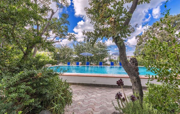 A swimming pool surrounded by lush greenery and trees, with a clear blue sky above. - Hotel Vittoria (Ischia)