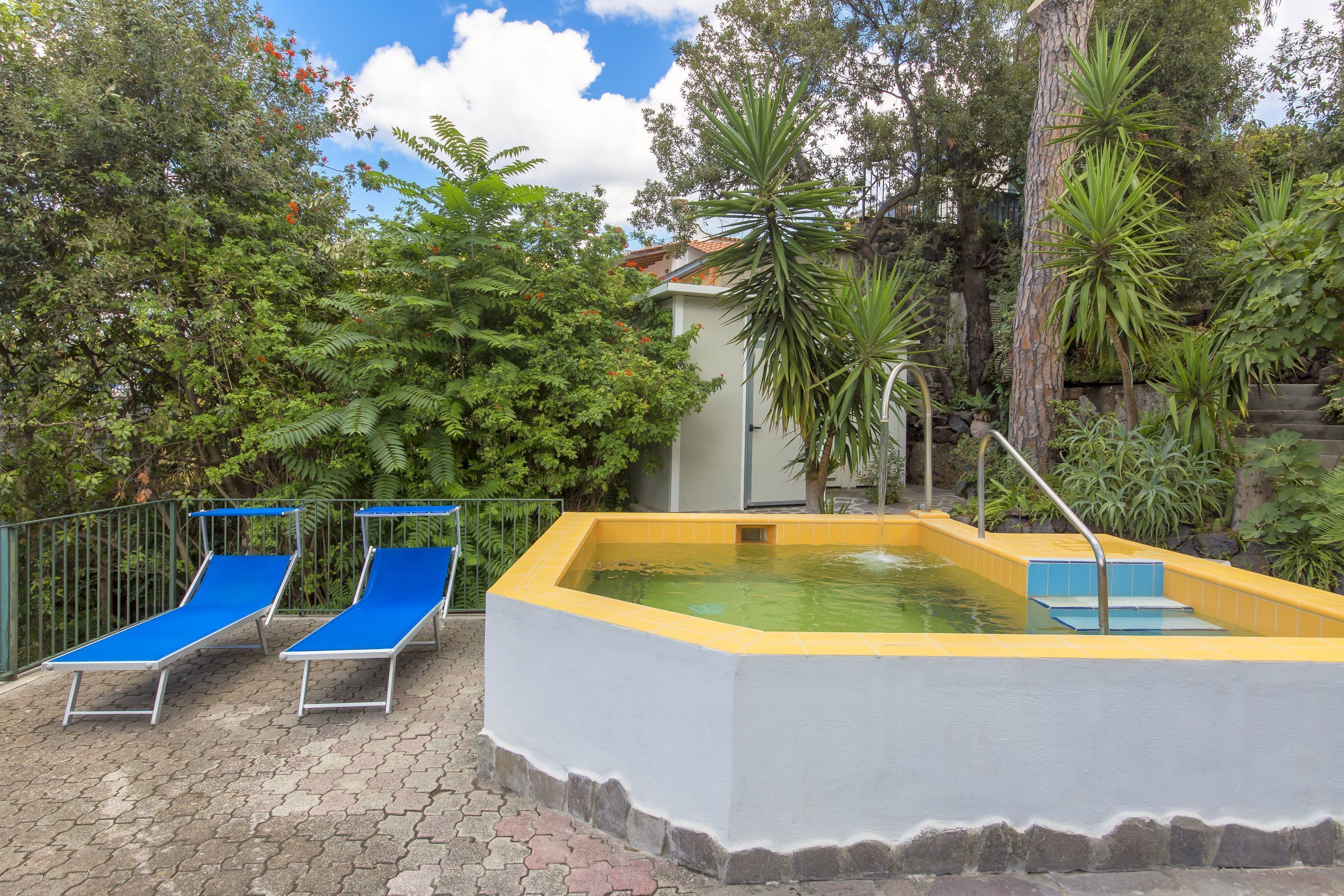 A swimming pool with two blue lounge chairs and a stone-tiled deck.