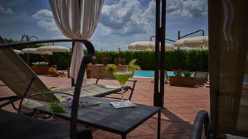 Een terras met lounge fauteuils, parasols en een zwembad.