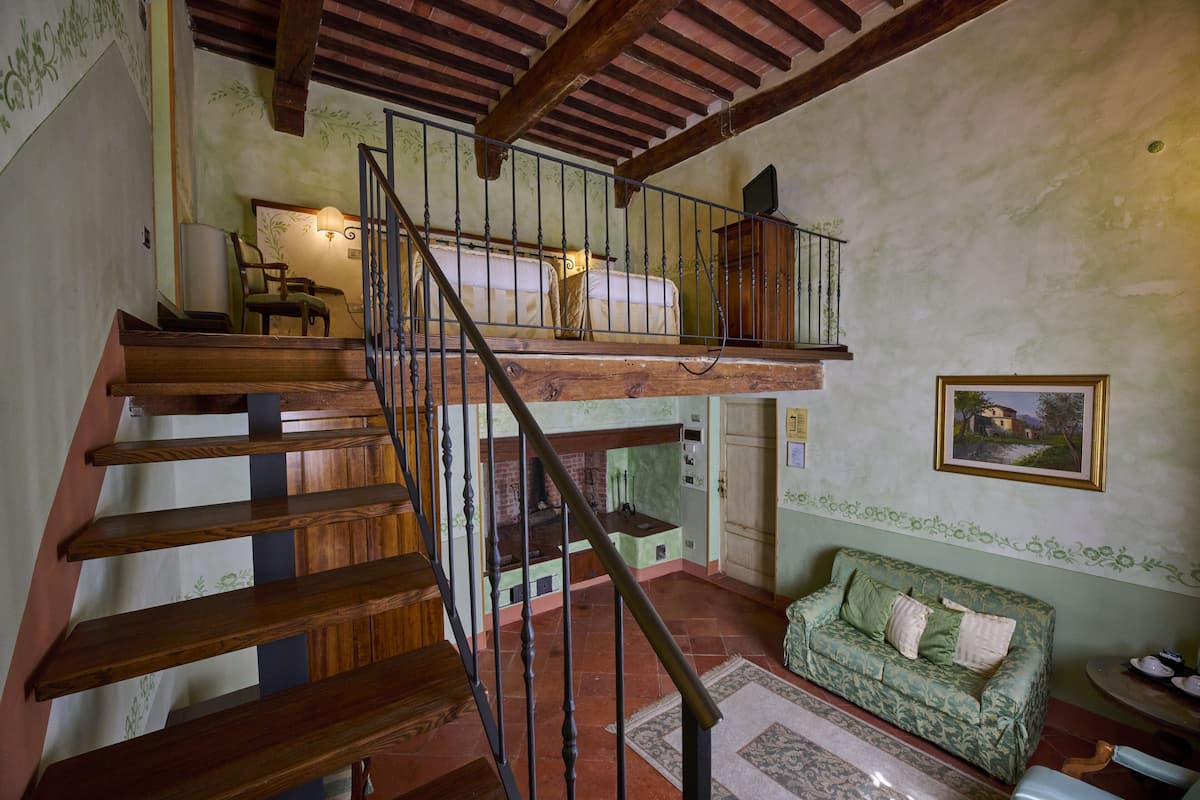 Un interior rústico con una escalera de madera, un sofá verde estampado y una chimenea.