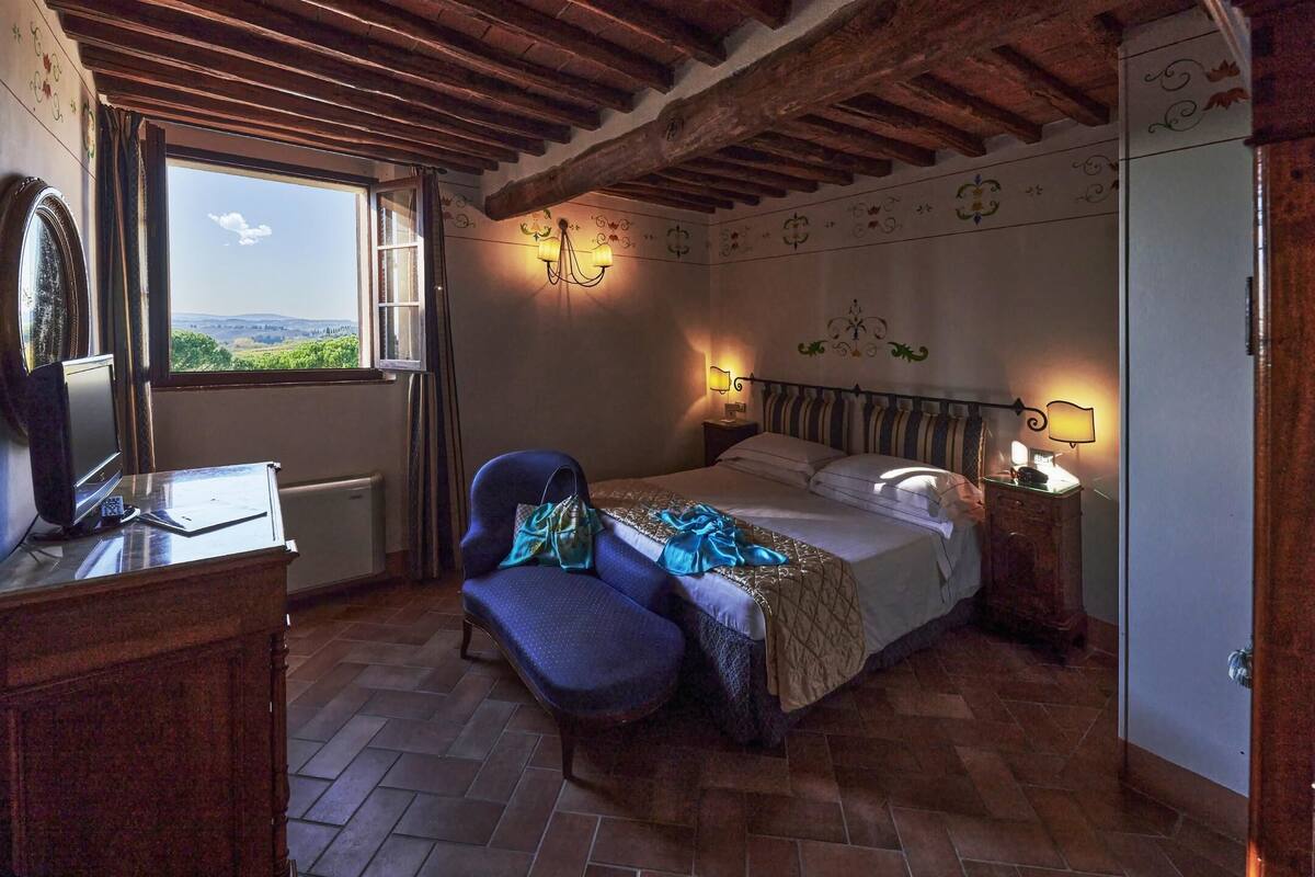 Un dormitorio con cama, una silla, un escritorio y ventana con vista al campo.