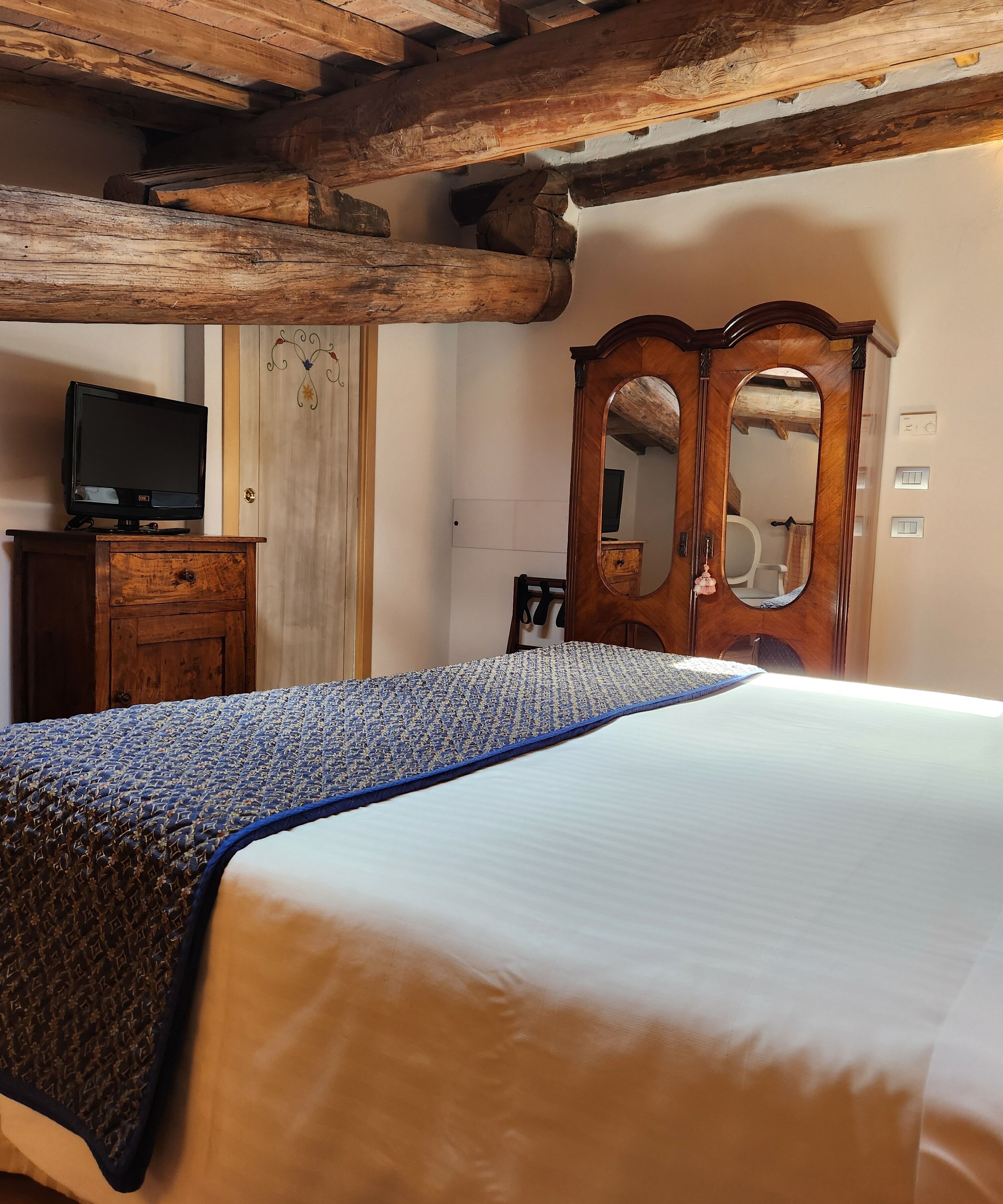 Un dormitorio con estructura de cama de madera, un televisor sobre un mueble de madera y un armario de madera con espejo.
