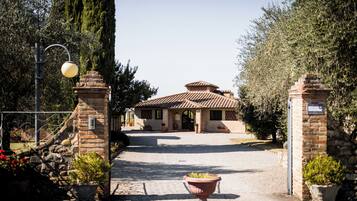 A building entrance with a paved driveway, stone pillars, and potted plants.