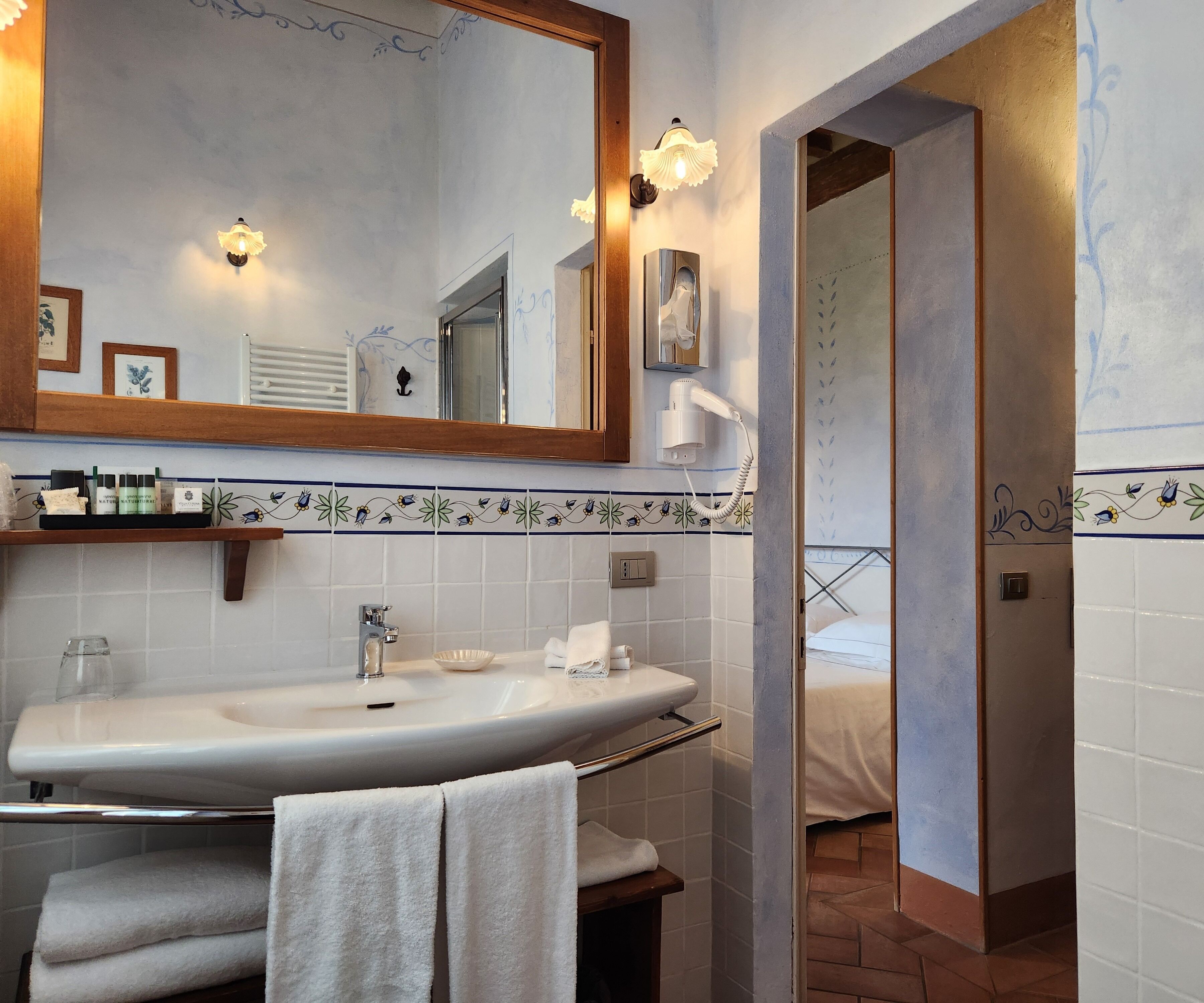Un baño con un espejo grande, un lavamanos, un secador de pelo y un perchero para toallas.