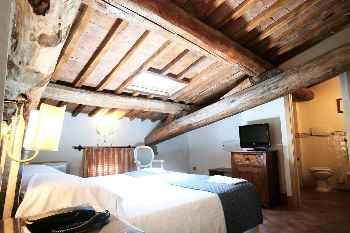 A rustic room with a wooden ceiling, a bed with a white bedspread, a desk with a telephone, and a television on a wooden cabinet.