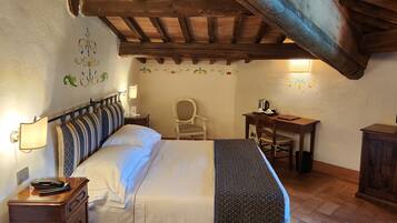 A bedroom with a large bed, a desk, a chair, and a small table with a lamp.