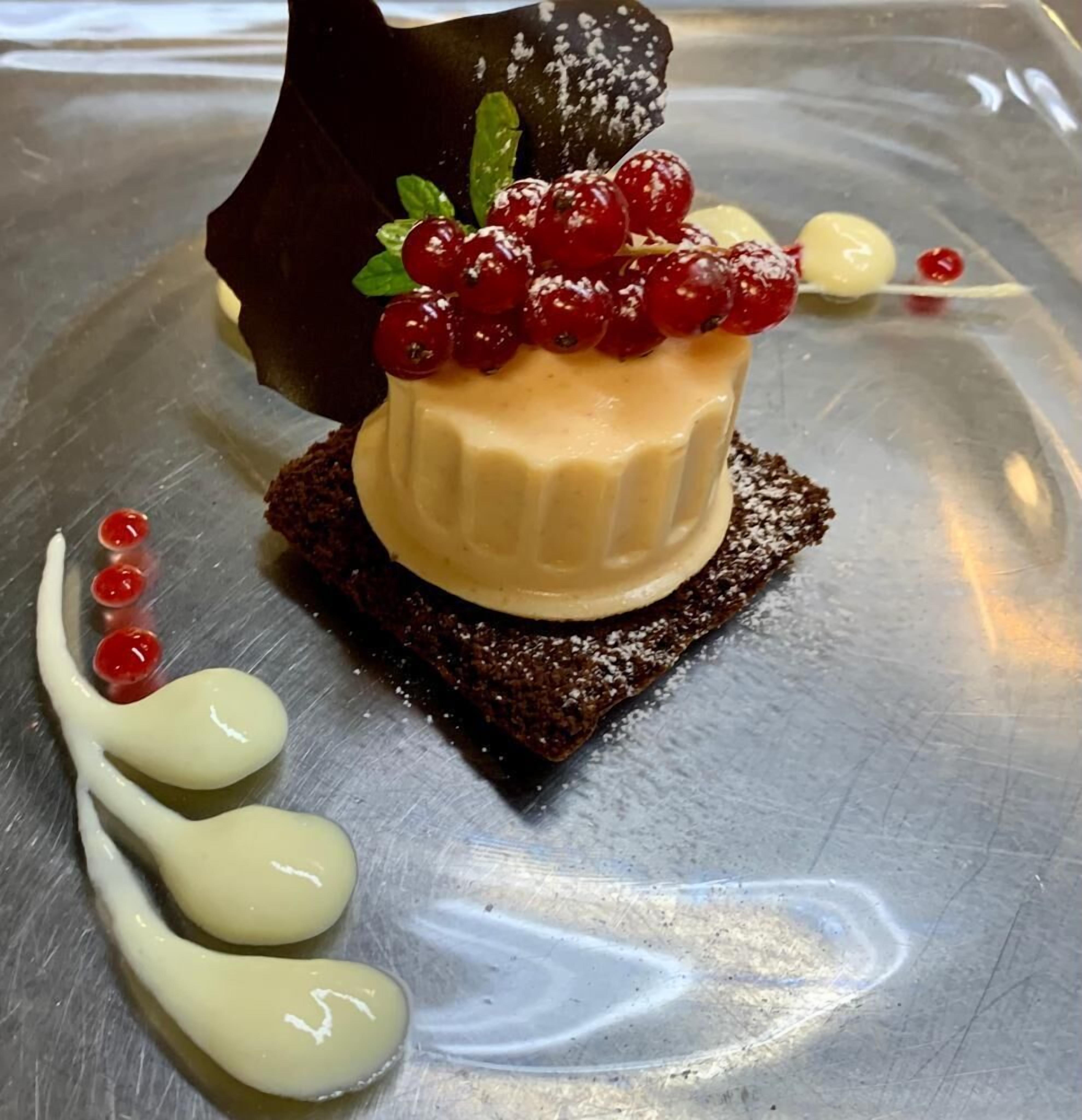 Un postre sobre un plato de metal, con una base de chocolate, un relleno cremoso y bayas rojas en la parte superior.