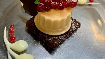Un postre sobre un plato de metal, con una base de chocolate, un relleno cremoso y bayas rojas en la parte superior.