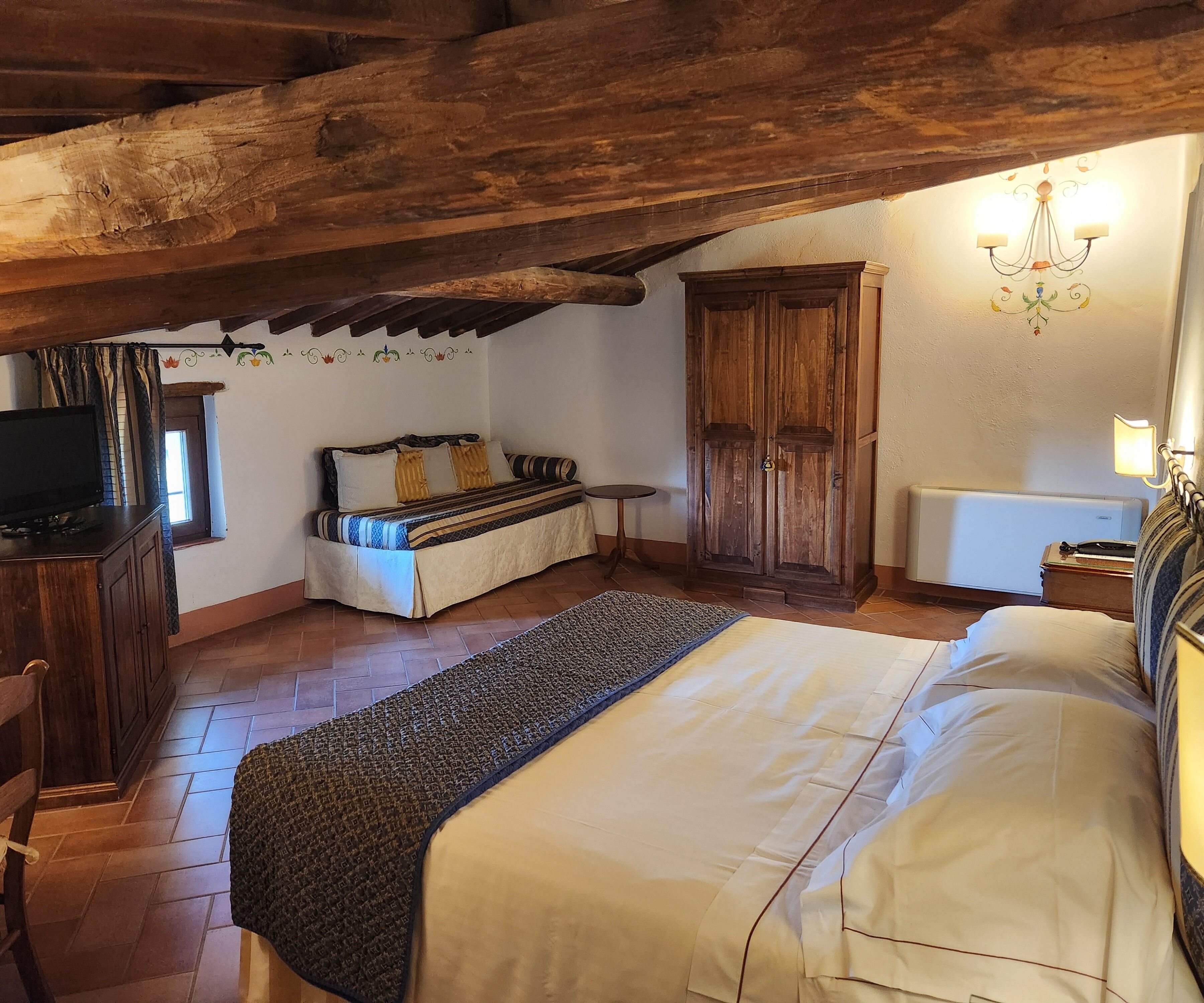 A cozy bedroom with a bed, a wooden wardrobe, a small table, and a television.