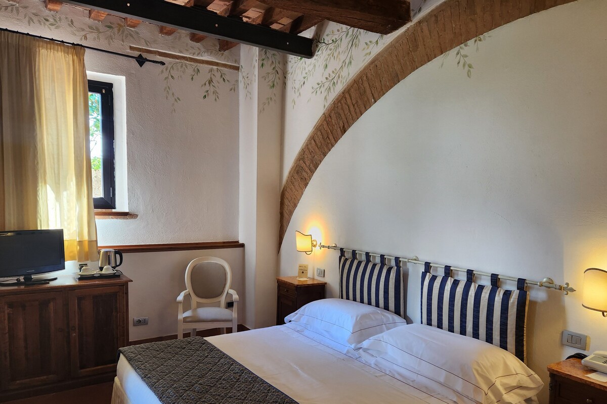 Une chambre à coucher avec un lit, un bureau avec une télévision, une chaise et une fenêtre avec des rideaux.