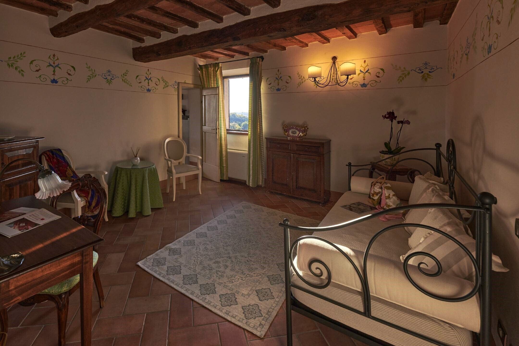 A cozy room with a bed, a table, a chair, and a small table with a green tablecloth.