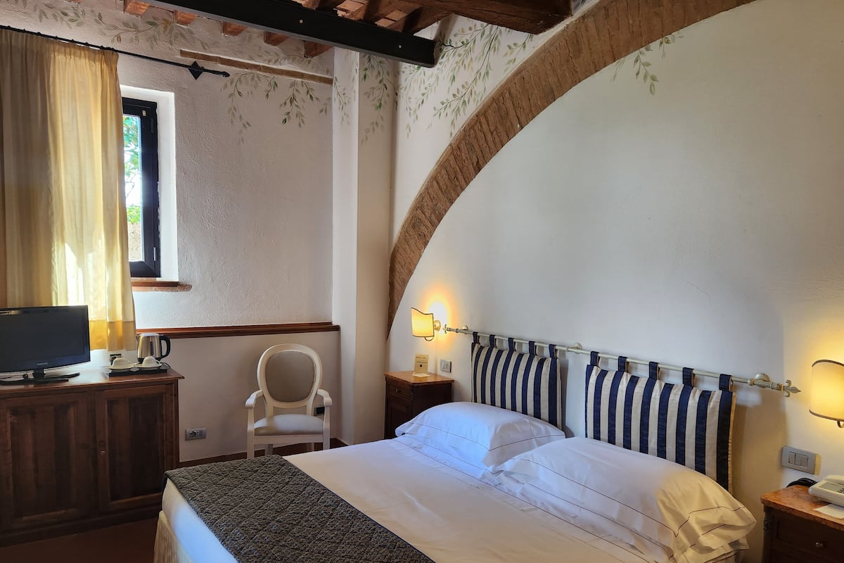 Un dormitorio con cama, escritorio con televisor, silla y ventana con cortinas.