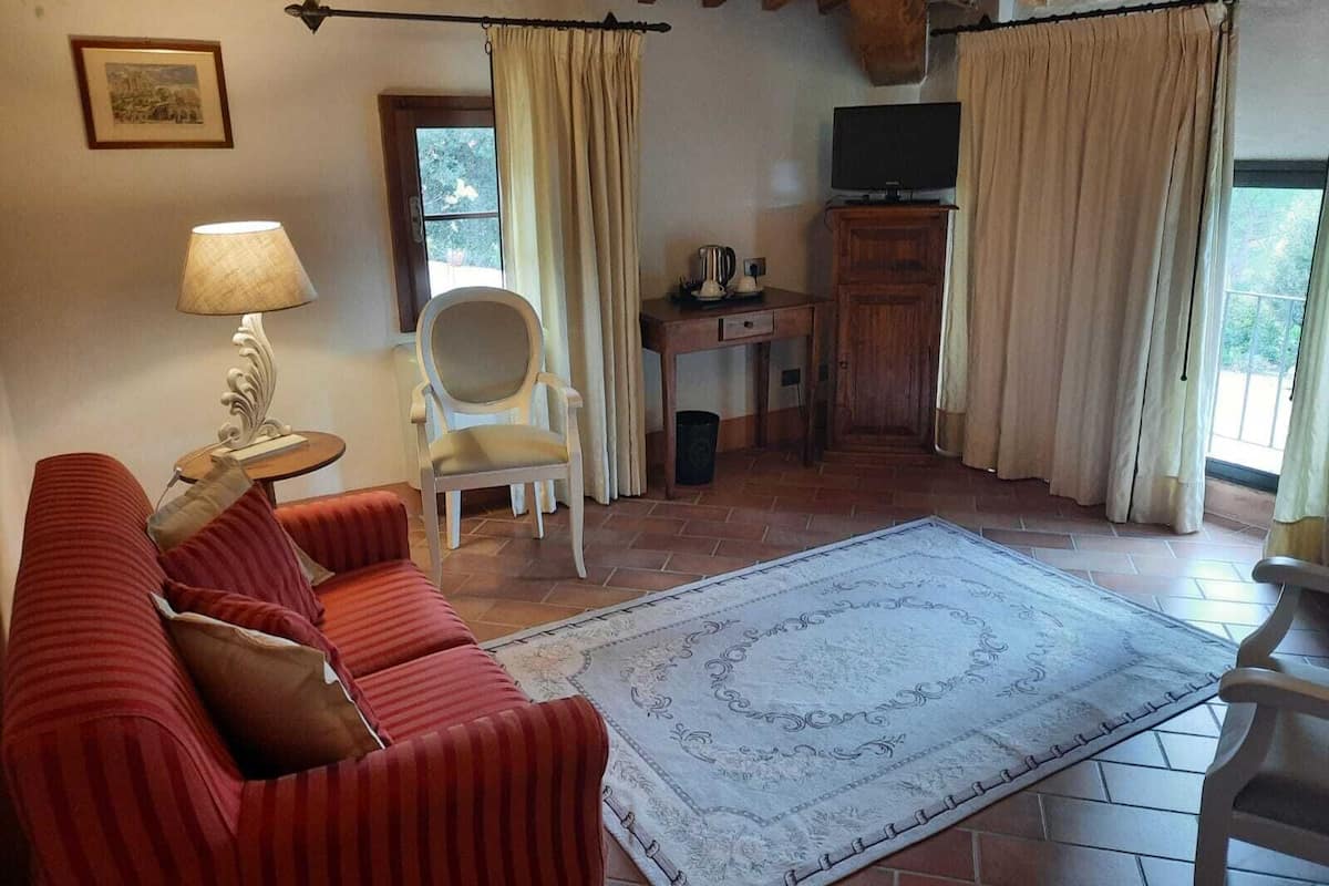 Una sala de estar con un sofá rojo, un sillón blanco, un escritorio de madera y una alfombra grande con estampado.