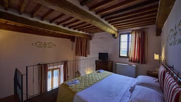 Une chambre à coucher avec un lit, des poutres en bois, un téléviseur, une fenêtre avec des rideaux et un radiateur.