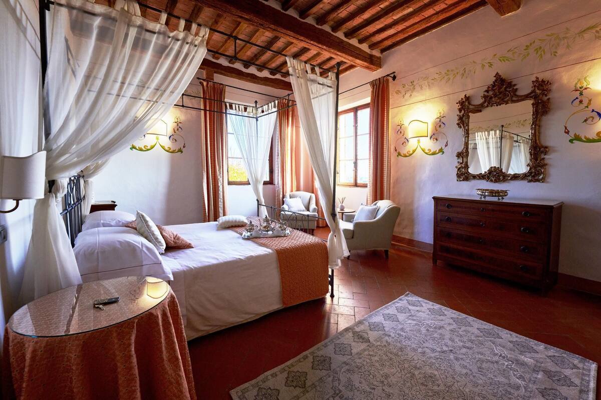 Un dormitorio con cama, mesita de noche, silla, cómoda y un espejo grande.