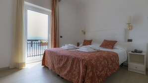 Habitación de hotel con una cama grande, una mesita de noche, una lámpara de pared y vistas al balcón.
