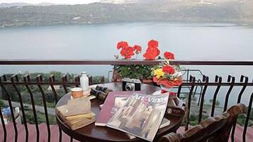 Una mesa con una revista, una cámara y un florero en un balcón con vista a un lago y montañas al fondo.
