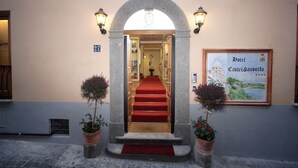 Entrada de hotel con alfombra roja, escalones de piedra y dos macetas.