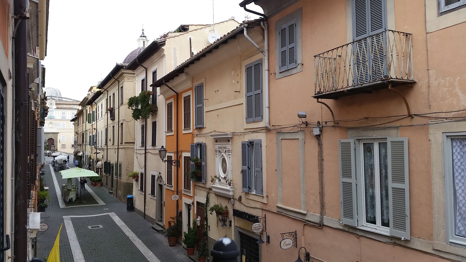 A narrow street lined with traditional buildings, some with balconies and potted plants.