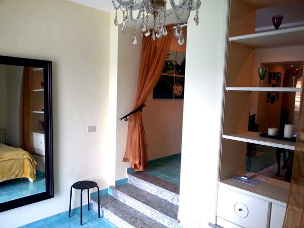 A bedroom with a bed, a small stool, a staircase, and a chandelier.