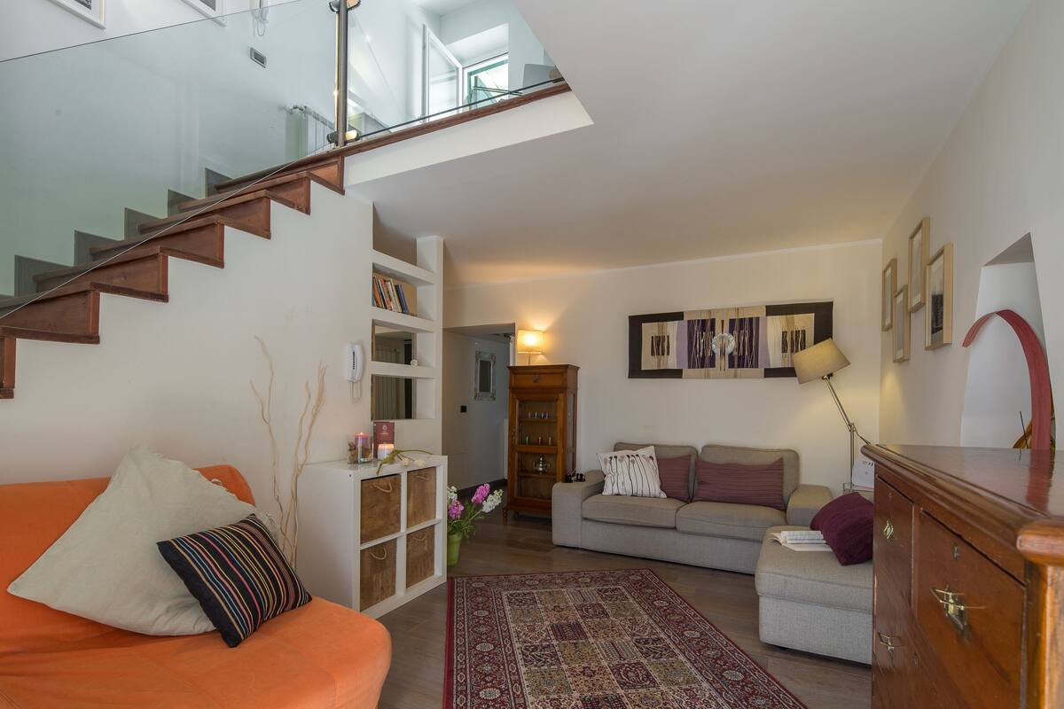 Una sala de estar con una escalera, un sofá, una mesa de centro y una estantería.