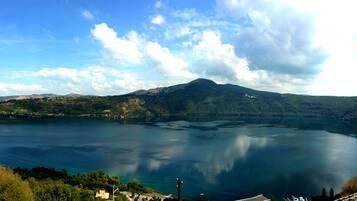 A panoramic view of a lake with a mountain in the background, surrounded by greenery and a few buildings.