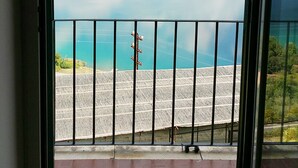 Vista desde un balcón con barandilla de metal, con vista a una masa de agua y colinas distantes.