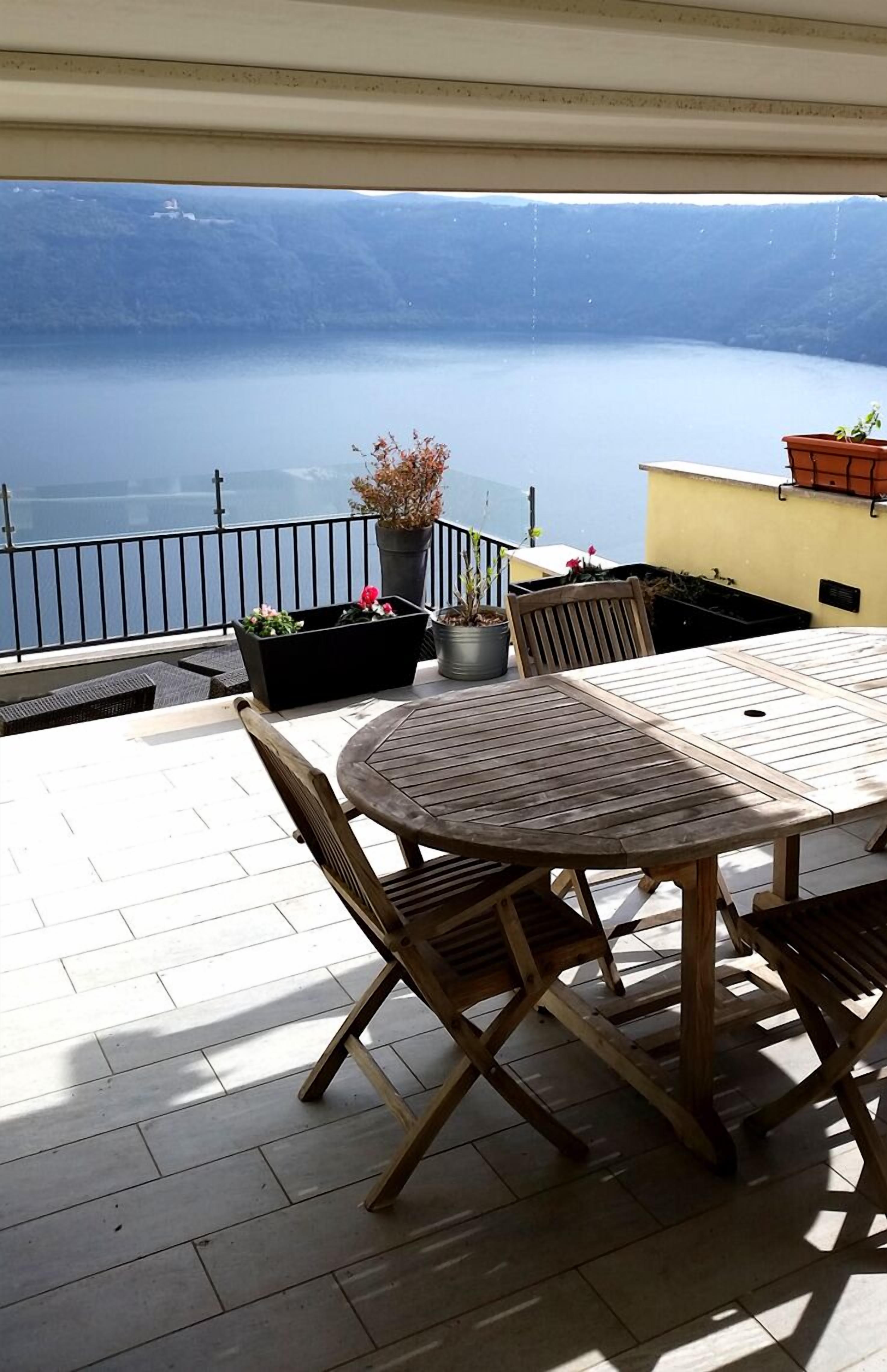 An outdoor patio with a round table and chairs, potted plants, and a view of the sea.