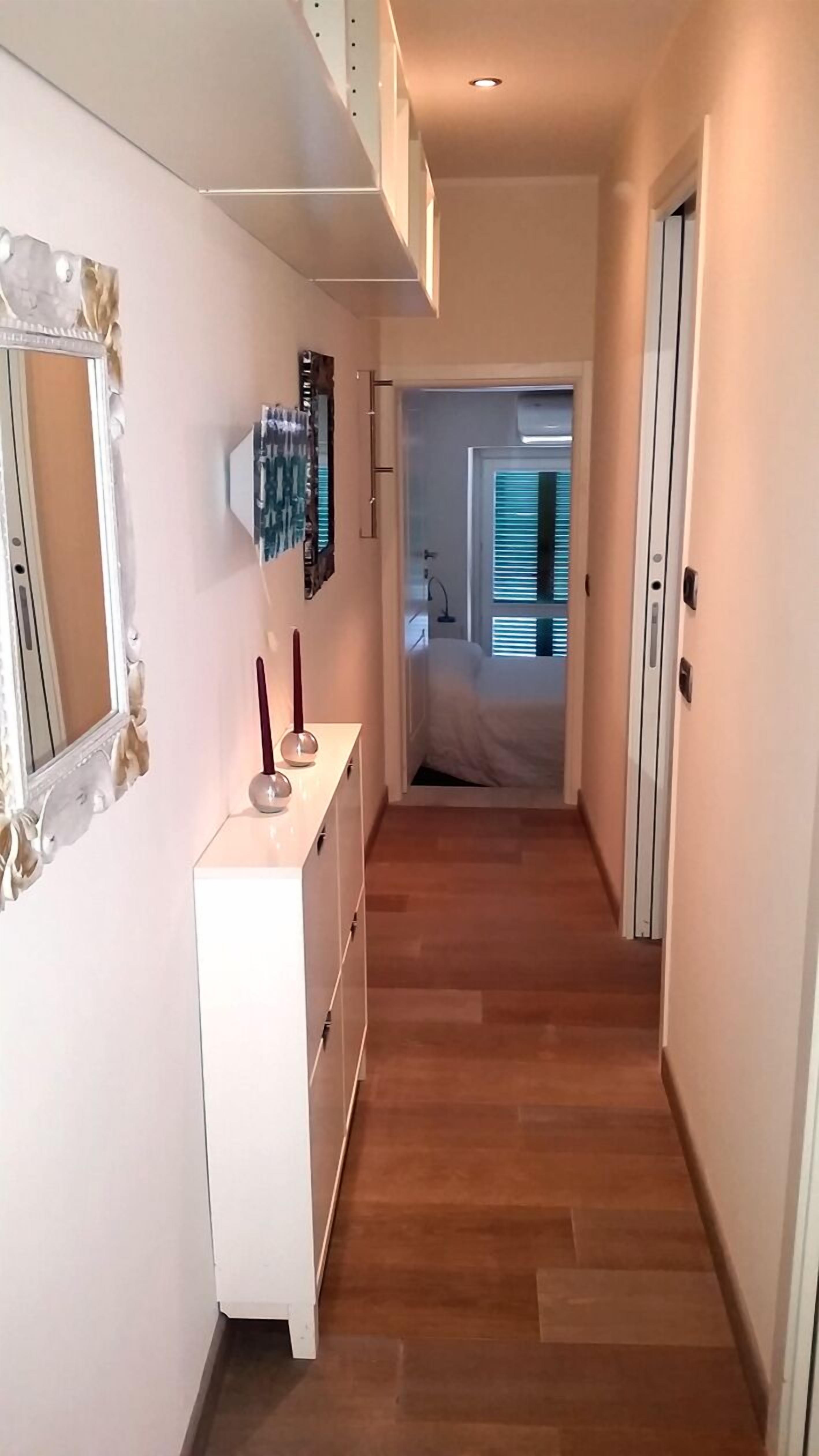 A hallway with a white dresser, a mirror, and a wall-mounted light fixture.