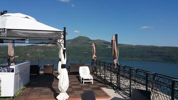 Una terraza con pérgola, sillas de descanso y vistas a un lago y colinas.