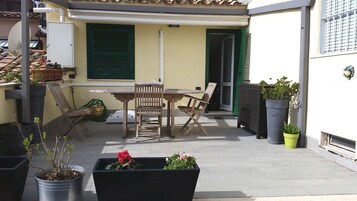 Un patio con una mesa y sillas de madera, plantas en macetas y un puerta corredera.