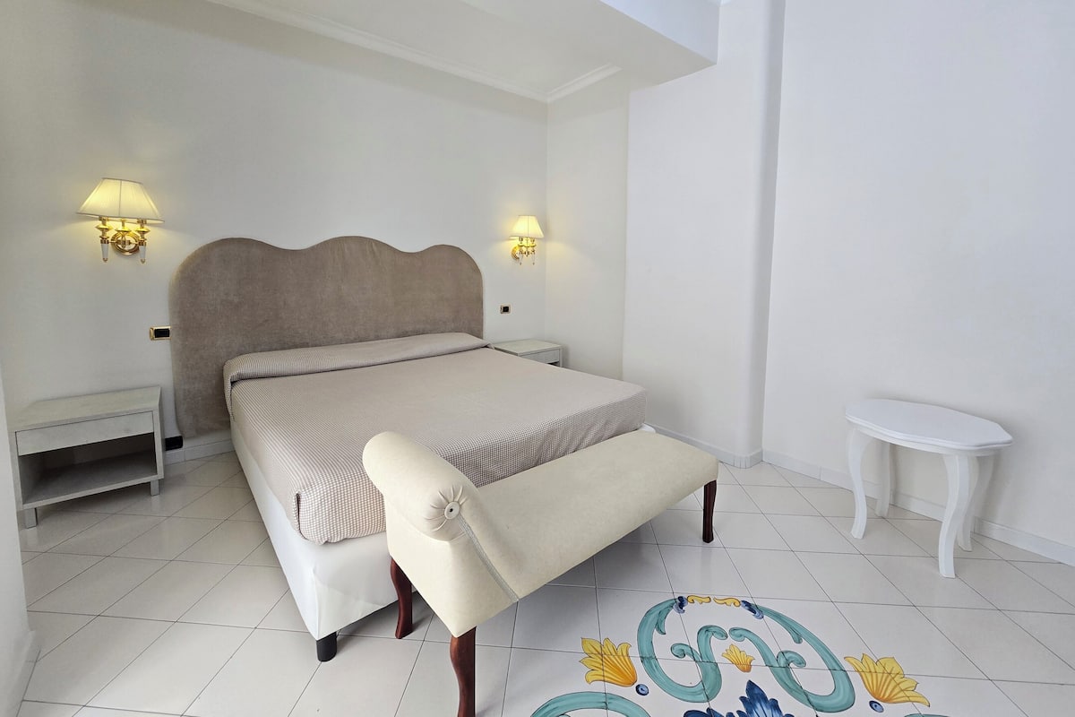 Een slaapkamer met een bed, nachtkastjes, een bankje en een klein rond tafeltje.