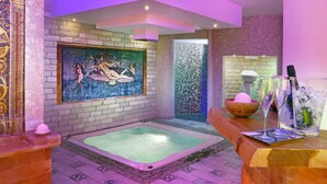 Un espace spa agrémenté d’un mur en mosaïque, d’une grande baignoire et d’un comptoir d’accueil en bois, orné d’un vase décoratif et de verres.