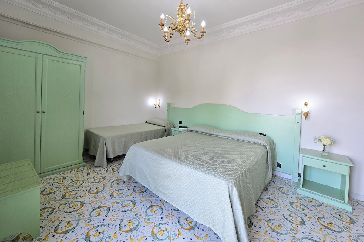 Een kamer met twee bedden, een garderobe, een pronkstuklamp en betegelde vloer.