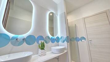 Ein modernes Badezimmer mit zwei großen Spiegeln, einem weißen Waschbecken und einer Duschkabine aus Glas.