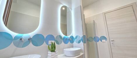 A modern bathroom with two large mirrors, a white sink, and a glass shower enclosure.