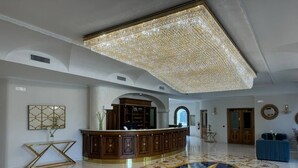 Un hall d’entrée spacieux avec un comptoir d’accueil central, un sol décoratif aux motifs complexes et un grand lustre.