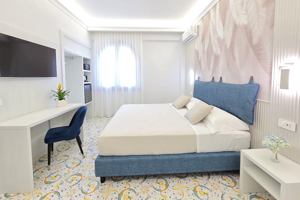 Een moderne hotelkamer met een bed, bureau, stoel, televisie en raam met gordijnen.