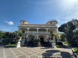 Un grand bâtiment à deux étages, doté d’une façade symétrique, de nombreux balcons et d’une entrée centrale avec des marches.