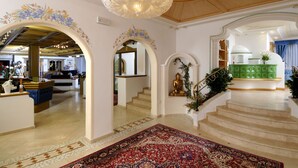 A grand foyer with a chandelier, ornate arches, a staircase, and a green console table. - Kristiania Pure Nature Hotel & Spa (Pejo)